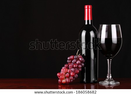 Wine Bottle and Glass of Red Wine with Fresh Grapes over black background.