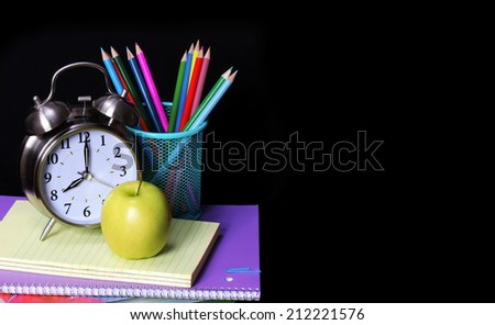 School Supplies over black background. Studies Accessories: an apple, colored pencils and alarm clock on pile of books.