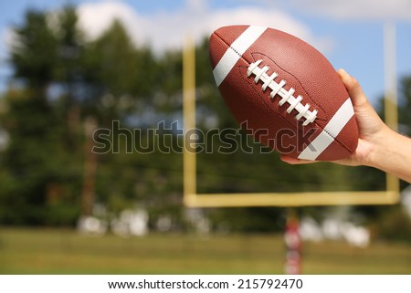 American Football in Hand over Field with Goal Post or Uprights