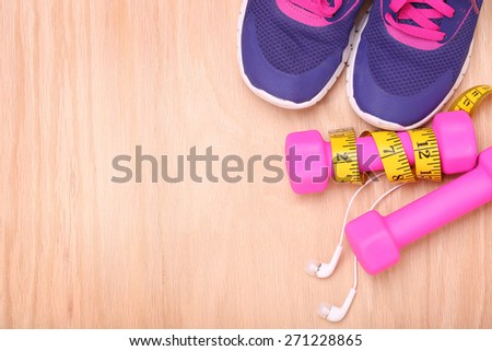 Sport equipment. Sneakers, dumbbells, measuring tape and earphones on wooden background