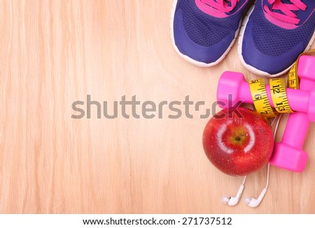 Sport equipment. Sneakers, dumbbells, measuring tape, apple and earphones on wooden background