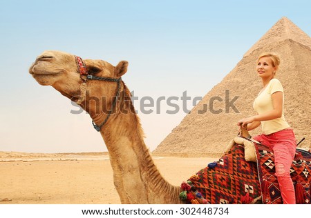 Tourist riding camel in Giza. Young blonde woman near Pyramid of Khafre, Egypt