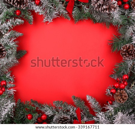 Border, frame from christmas tree branches with pine cones and holly berries over red