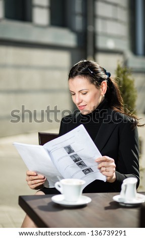 woman in a cafe on the street with a cup of coffee, read the papers