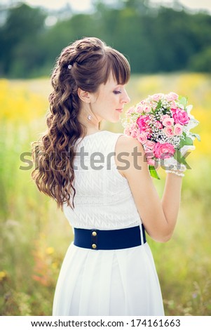 portrait of a girl in a white dress with a bouquet of flowers in a field on a background of yellow flowers and green trees.