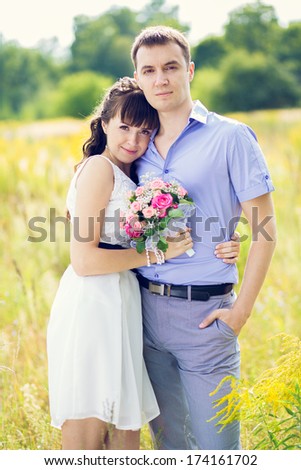 portrait of a boy and a girl with a bouquet of standing against the yellow fields and green trees