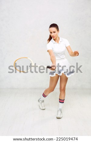 Beautiful girl in tennis clothes, brandishing a tennis racket on a white background, textured wall.