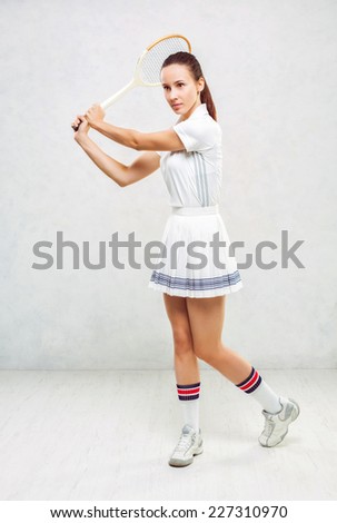 Beautiful girl in tennis clothes, brandishing a tennis racket on a white background, textured wall.