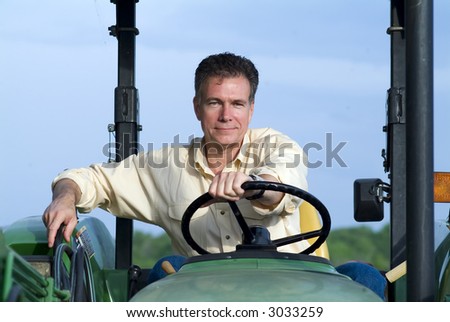 Handsome mature male sitting comfortably on a big green tractor smiling confidently.