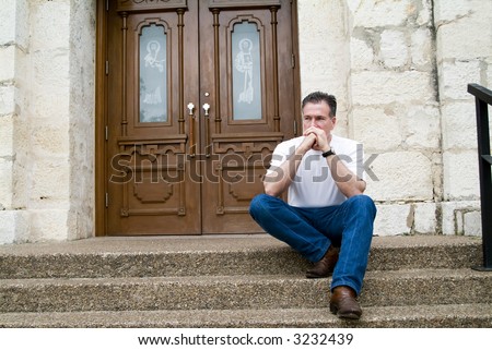Man sitting on the steps of a church with an anxious expression on his face and in his body posture.