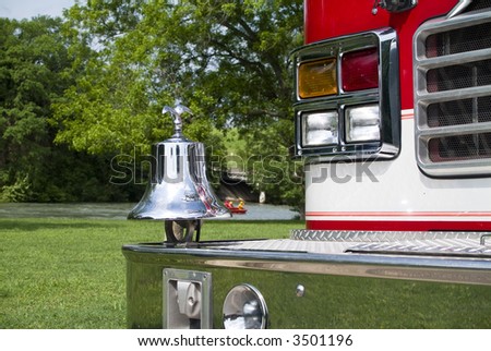 A close up of a fire truck\'s bell and front bumper with the rescue team performing a water rescue drill in the background.