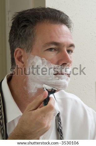 A man looking in the mirror in the process of shaving.