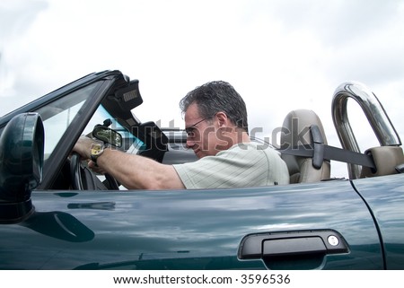 A man in a convertible sports car driving with the top down and passing a car.