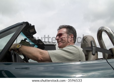 A man in a convertible sports car driving with the top down and passing a car.