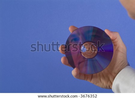 A man holding a DVD or CD with his face reflecting back at him with available copy space.