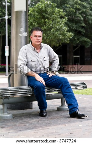 A man sitting on a bench at a downtown bus stop.