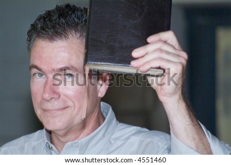 A man holding a book which could be a bible up in the air.