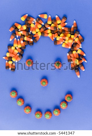 A smiley face made with candy, with candy corn hair taken on a blue background.