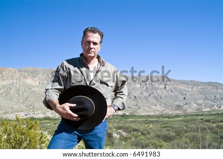 A man standing with his hat in his hand in a gesture of respect for the rugged beauty surrounding him.