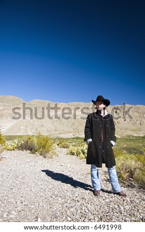 A woman dressed in a black coat and black western hat observing her surroundings.
