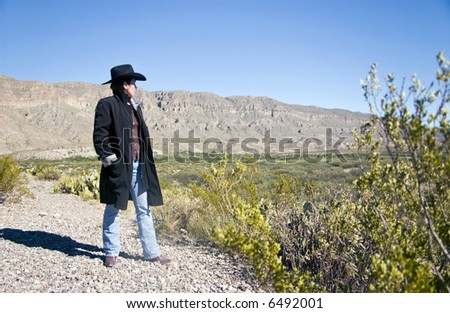A woman dressed in western attire looking out at the rugged terrain laid out before her.