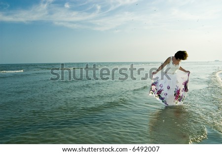 A woman standing in the surf spreading out her wet skirt.