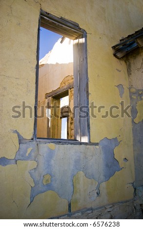 View through the window of an old abandoned building to a window and door of another room.