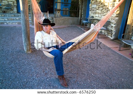 A man dressed in a cowboy hat and boots resting in a colorful hammock.