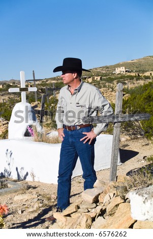 A man dressed in western attire standing in the middle of an old graveyard.