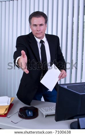 A man standing in front of a desk with his hand extended as if to greet someone.