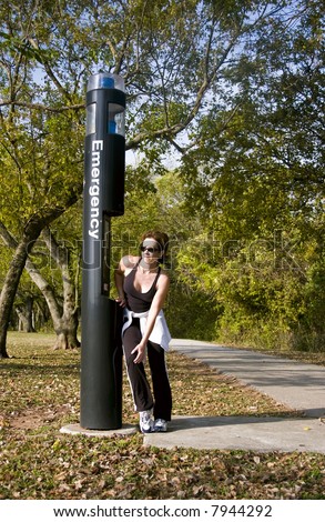 A woman standing by an emergency call box holding her knee as if in pain.