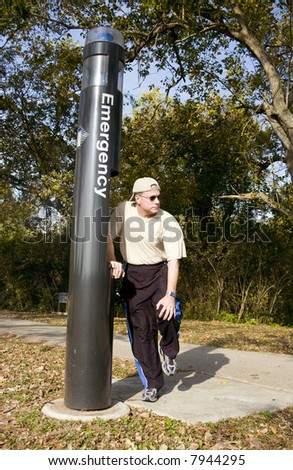 A man standing by an emergency call box holding his knee as if in pain.