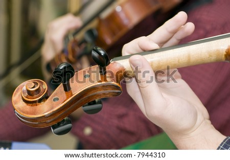 A close up of a young violinists\' hand and the pegs and peg box of the violin.