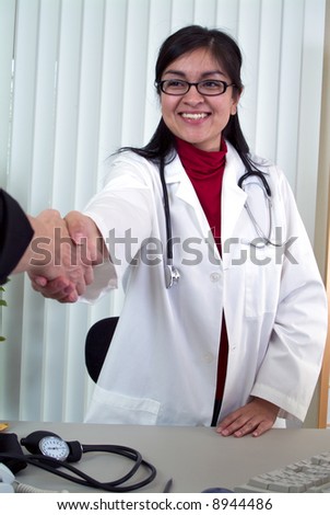 A smiling young woman dressed as a doctor shaking someone\'s hand.