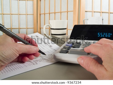 A woman\'s hands holding a pen and working with a tax form and adding machine.