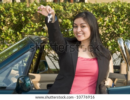A pretty, smiling, young woman standing in front of a sports car holding out a set of car keys.