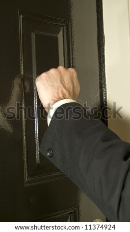 A man knocking on a newly painted shinny door with his fist.