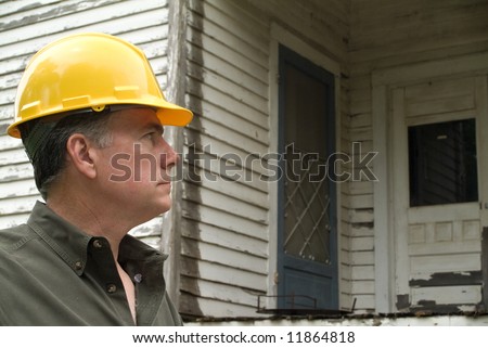 A man in a hard hat looking at an old rundown house.