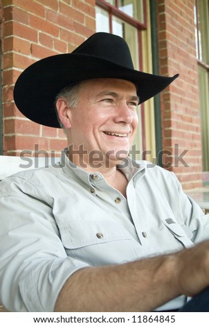 A man sitting on a porch wearing a cowboy hat with a big happy smile on his face.