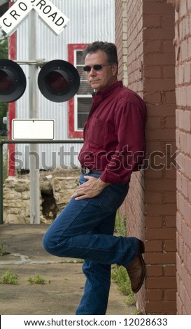 A man leaning up against a red brick wall with a railroad crossing warning signal in the background.