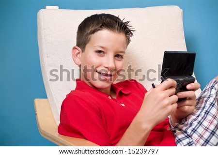 A boy sitting in a chair, holding an electronic video game device.