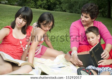 A woman with three teens or preteens sitting outside as if engaged in bible study.