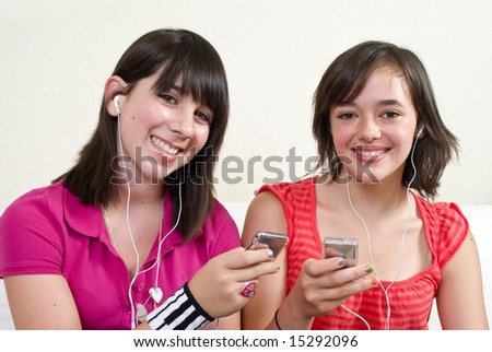 Two friends with big smiles listening to music on their portable music players.