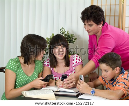 A woman reaching for a cell phone in the hands of one of three kids at a study table.