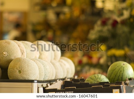A stack of cantaloupes and watermelons in a grocery. Focus on the foreground.