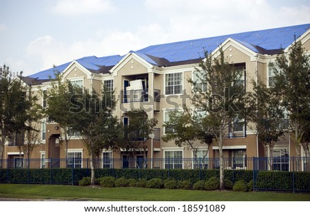 Blue tarps covering the damaged roofs of an apartment complex in the aftermath of a hurricane.