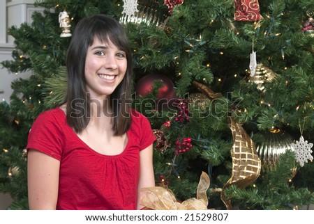 A lovely young girl with a sweet smile sitting by a Christmas tree.