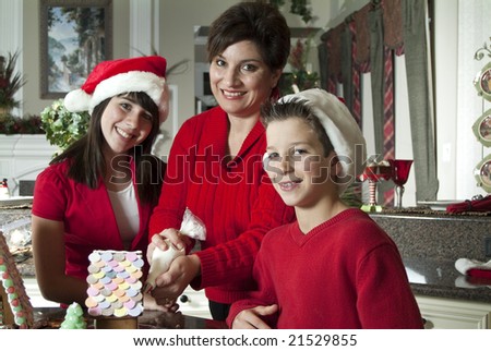 A mother and her two children working together to decorate a gingerbread house.