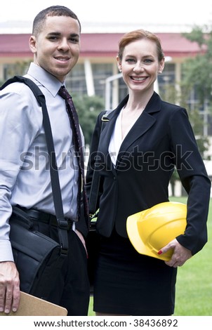 Two business people, of which one is a woman holding a hardhat, smiling for the camera.