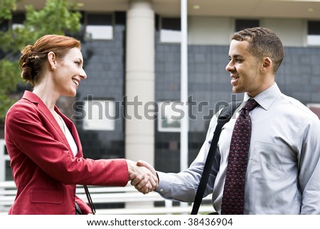 Two business people outside a downtown building greeting each other with a handshake.